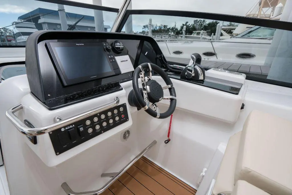 Boat cockpit with a steering wheel, touchscreen display, engine controls, and leather seating, set in a marina environment.